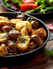 Baked potato with mushrooms and herbs in iron cast pan on wooden table