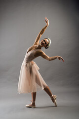 Beautiful ballet dancer posing on pointes on light grey studio background