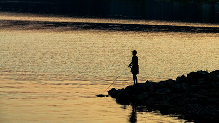The girl is fishing on spinning. Sunset Czech Republic Lipno lake.