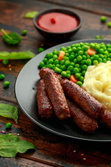 Vegetarian vegan sausages with mashed potato and green peas in black plate