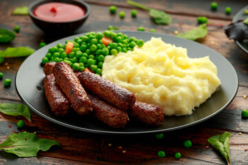 Vegetarian vegan sausages with mashed potato and green peas in black plate