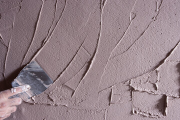 The plasterer levels the uneven plaster on the wall with a small spatula. Close-up