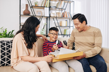 Cheerful Vietnamese parents giving son big box with modern headphones inside for birthday