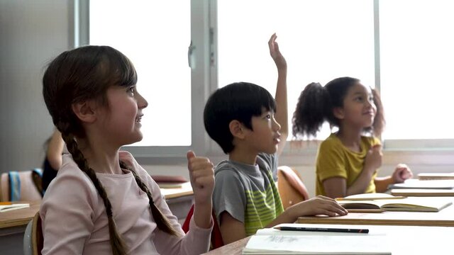 Elementary age Asian student boy raised hands up in Q & A class. Diverse group of pre-school pupils in elementary age in education building school. Volunteering and participating classroom concept.