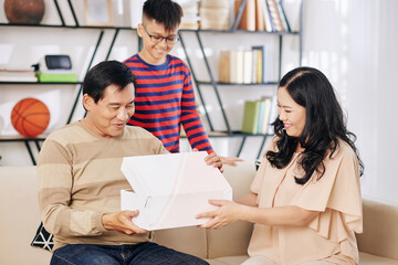 Mature Asian woman giving birthday present from her and their son to excited husband