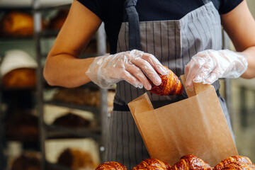 Seller placing freshly baked crispy golden croissants in a paper bag