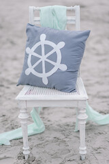 Elegant vintage white chair with pastell green cover, bright streering wheel ship on grey pillow, small flowers basket on the beach, northsea, Sankt Peter-Ording. Outdoor wedding day decoration.