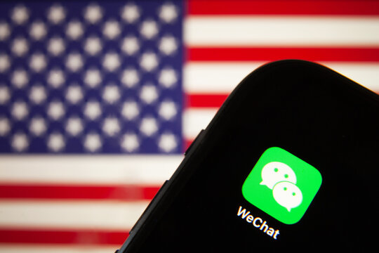 Cellphone With WeChat Icon In Front Of The Flag Of America. USA President Donald Trump Bans Apps Of China Due To The National Security 