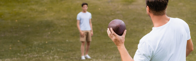 panoramic concept of father holding rugby ball near teenager son in green park