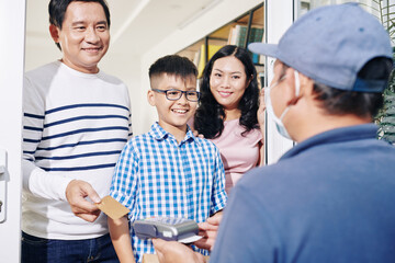 Cheerful Vietnamese family receiving package and paying for delivery