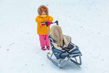 little girl with sleigh at snowed winter day