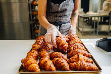 Gloved hand placing freshly baked crispy golden croissants on a tray to cool