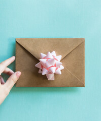 Kraft envelope with pastel pink bow in woman's hand on turquoise background. 