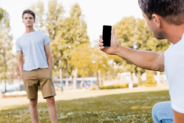 selective focus of father holding smartphone and taking photo of teenager son in park