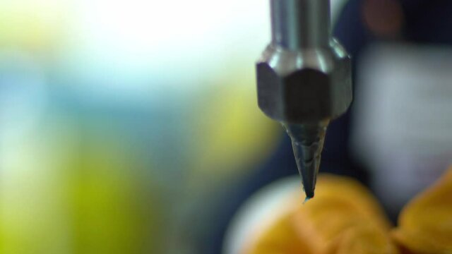 The factory worker in yellow glows putts automotive part detail in production machine filling with lubricant it's edges.
