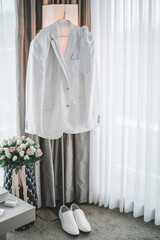 Grooms white wedding suit with shoes and bride bouqet hangs on a lamp. Getting ready morning concept.