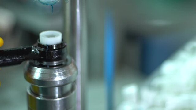 The factory worker in yellow glows putts automotive part detail in production machine filling with lubricant it's edges.