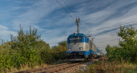 Blue electric engine and expres passenger train near Budweis station in summer