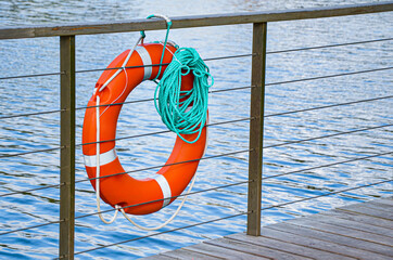 Red emergency lifebuoy with turquoise rope on pier near sea. Closeup of lifebuoy on dock. Rescue...