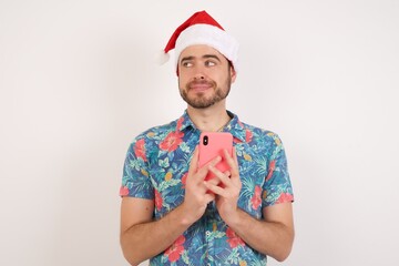 Funny Young caucasian man wearing hawaiian shirt and Santa hat over isolated white background holds telephone hands reads good youth news look empty space advert