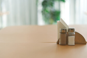 Salt and pepper stays on restaurant table with napkin stand, heavy blurred background, selective focus