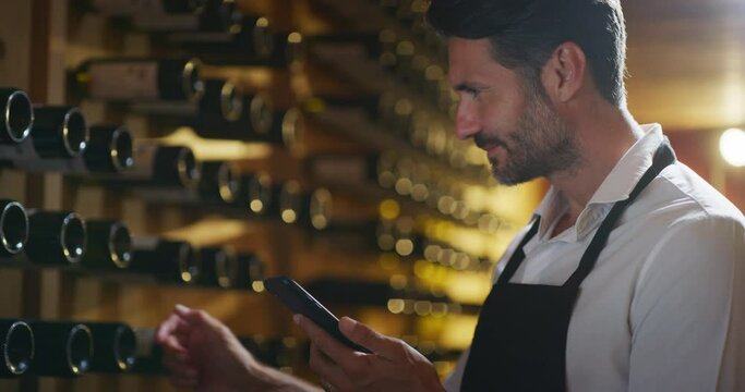 Modern farmer or winemaker is using winery online commerce applications on a smartphone for checking customer service and selling orders summary of his wine production in a wine cellar.
