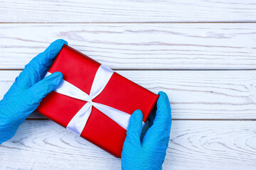 gloved hands hold a red gift box with a ribbon on a wooden background. Concert of epidemics, pandemics
