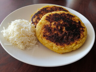 Plantain arepas with white grated cheese on white plate