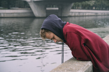 Fototapeta na wymiar portrait of sad unhappy lost frustrated young boy / teenager in hoodie by the river