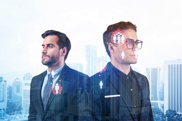 Fototapeta premium Two handsome young SMM specialists thinking about development of social media marketing strategy to achieve business goals. Hologram icons over Kuala Lumpur background.