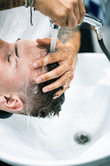 Selective focus of barber washing hair of young man in barbershop