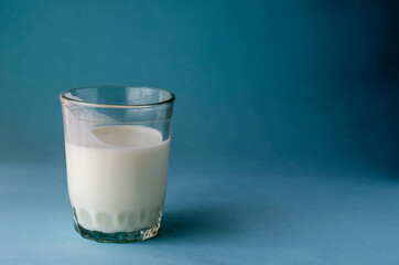 Glass cup partial of kefir on blue background.