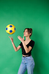 Young girl's throwing up a soccer ball. Woman tossing a yellow football ball using her hands. Standing against green chromakey.