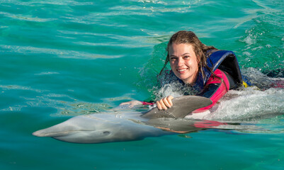Smiling woman swimming with dolphin in blue water. © Uryadnikov Sergey