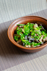 Salad with pickled mushrooms and green onions in a clay bowl.