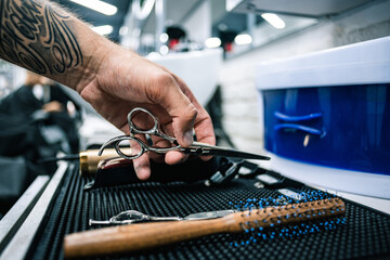 Selective focus of tattooed barber taking scissors from table in barbershop 