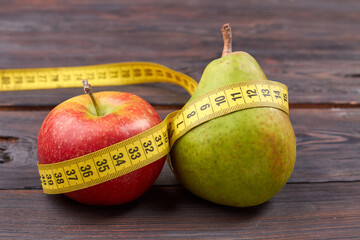 Fresh pear and apple with measure tape. Healthy diet concept. Fruits on wooden table.