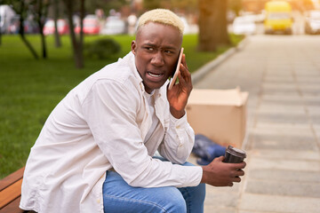 Obraz premium Unpleasant phone call, worried anxious man talking mobile phone sitting bench summer park