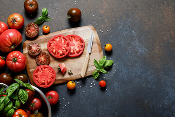 Fresh colorful ripe fall or summer heirloom variety tomatoes with knife and chopping board over dark blue table background. Harvest and cooking tomato sauce concept.
