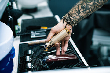 Selective focus of tattooed barber holding hair clipper near equipment in salon 