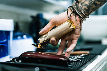 Cropped view of tattooed barber holding hair clipper near equipment 
