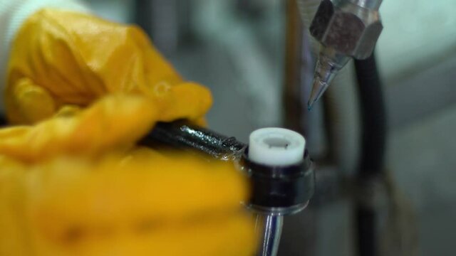 The factory worker in yellow glows putts automotive part detail in production machine filling with lubricant it's edges.