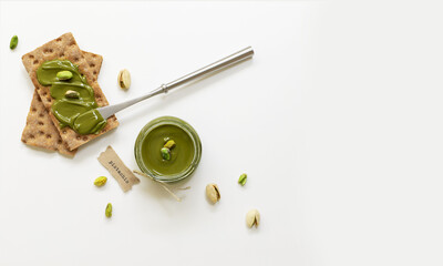 Pistachio nut butter in a glass jar. Homemade raw organic pistachio nuts paste on white background. 
Healthy natural food concept. Top view.