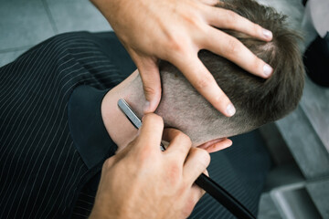 Overhead view of barber trimming neck of young client during haircut in barbershop 