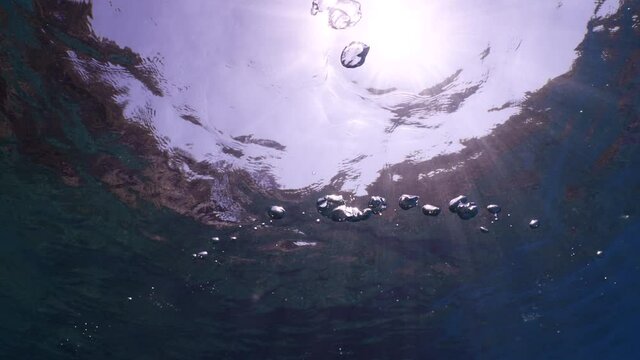 air bubbles underwater in blue water moving strange some in focus some out of focus making nive background shapes with sun rays and sun shine