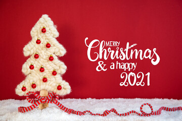 English Calligraphy Merry Christmas And A Happy 2021. White Fabric Christmas Tree With Snow And Red Background. Decoration Like Red Ribbon