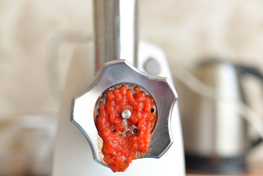 the process of grinding red tomatoes in a meat grinder