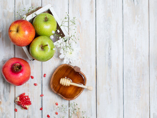 Rosh Hashanah Jewish New Year holiday concept. 
Creative layout of traditional symbols - apples, honey, pomegranate isolated on white wooden background, top view, copy space.