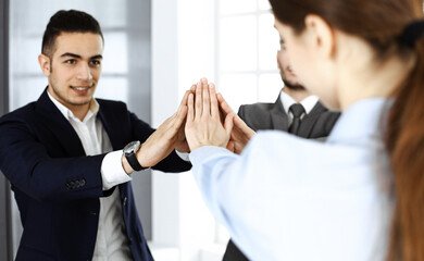 Business people group showing teamwork, joining hands and giving five to each other in modern office. Success concept