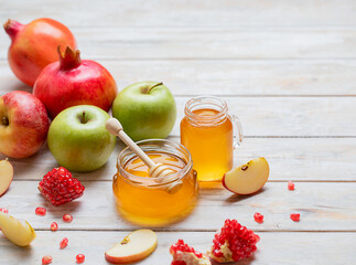Rosh Hashanah Jewish New Year holiday concept with traditional symbols - apples, honey, pomegranate on white wooden background. Copy space.